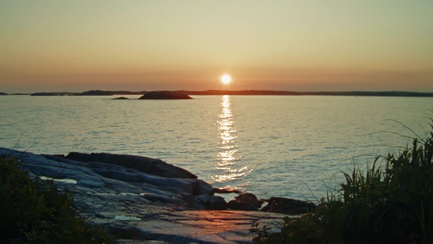 Light ocean waves roll gently against the rugged coast of Nova Scotia, with the sunset and distant islands creating a stunning cinematic seascape. Canada. Cinematic shot of scenery landscape