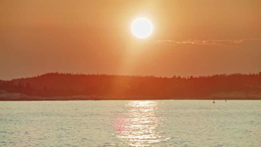 Soft waves caress the rocky coast of Nova Scotia at sunset, with distant islands and a glowing horizon adding to the cinematic beauty of the scene. Canada. Cinematic shot of scenery landscape