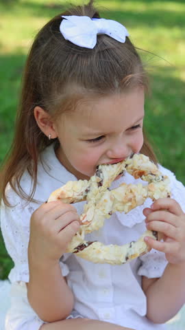 woman and girls,mother and daughters are having picnic.happy woman with kids eating pastry products on blanket in park.bright white clothes, sunny summer day.happy smiling sisters eating pretzel.