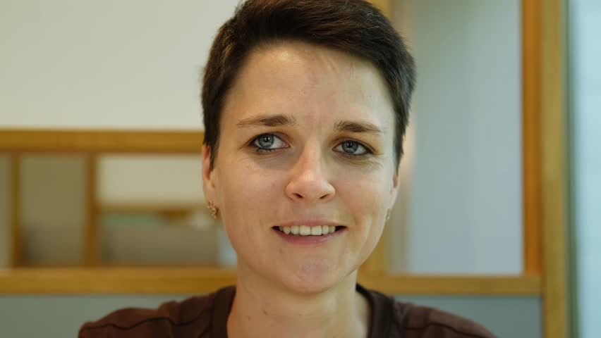 A young woman with stylish short haircut is sitting in a cafe and biting a delicious fresh hot meat burger with cheese. Girl in a cafe enjoying a break alone with cheeseburger. Close view