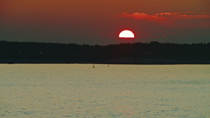 The sun sets over Nova Scotia rugged coast, casting soft light on waves rolling gently onto rocks, with distant islands completing the cinematic seascape, Canada. Cinematic shot of scenery landscape