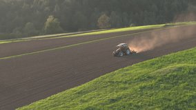AERIAL: Tractor ploughing an agricultural field on a sunny hillside, with late afternoon sun casting a warm glow over landscape. Machinery kicks up dust while preparing the soil for next crop season. - Powered by Shutterstock - Get 15% off with code: PIKWIZARD15