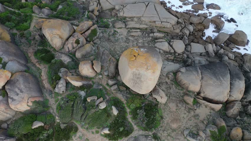 Aerial view of stormy waves crashing on rough boulders at a beach with mountains in the background, Cape Town, South Africa.