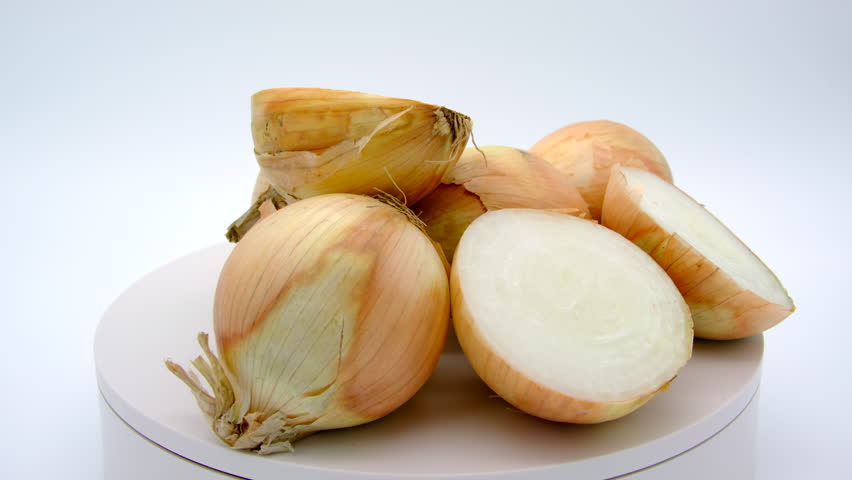 Pile of large unpeeled and some sliced in half fresh harvested yellow onions from local farm slowly spinning or rotating on turntable against white background