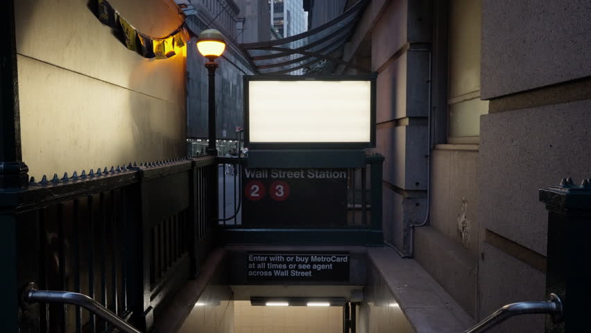 A subway entrance to the Wall Street Station, featuring the 2 and 3 train lines. The entrance is dimly lit with a glowing street lamp above, creating a contrast with the dark, narrow alleyway.