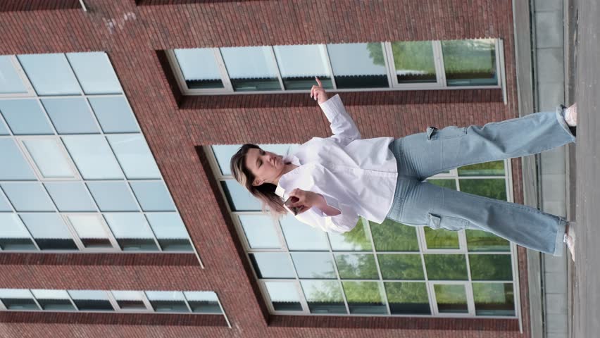 young woman performs an energetic dance in front of a modern building, her expression joyful and lively. This image highlights the spirit and dynamism of urban dance as a form of self-expression.