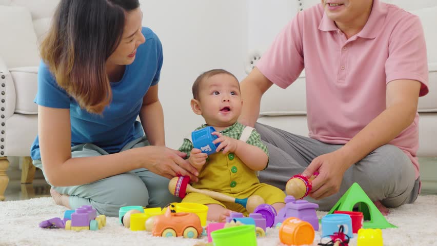 A family of three, a man and two women, are playing with toys on the floor. The baby is holding a toy truck and the parents are clapping. Scene is happy and playful	
