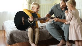 Happy dad teaches his cute son to play the guitar while sitting on the sofa in the living room at home. Happy Father's Day. Father teaching his child to play guitar. Kid Learning music skill - Powered by Shutterstock - Get 15% off with code: PIKWIZARD15