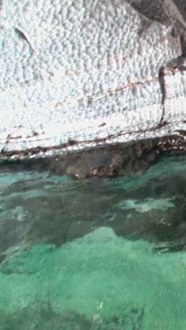 Serene Waters Under Rocky Cliffs at Sunset on Coastal Adventure. Tranquil aquatic scene unfolds as sunlight reflects off crystal-clear water, highlighting rocky formations along shoreline at sunset.