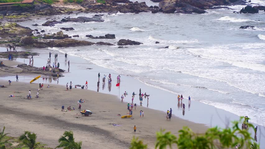 Wide angle aerial drone shot view from Chapora fort showing vagator beach with crowd of people enjoying the huge waves, sand, white foam during overcast cloudy monsoons