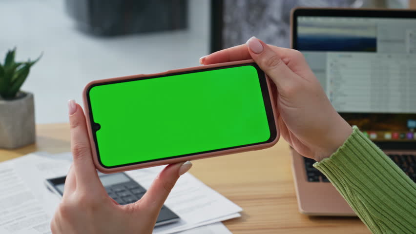 Student hands holding mockup smartphone watching social media at home closeup. Woman browsing content on green screen horizontal cellphone. Unknown freelancer looking video on chroma key mobile phone