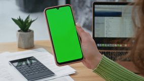 Closeup hand holding mockup cellphone in light office. Unrecognizable woman watching green screen smartphone turning on video content at home. Student browsing social media at chroma key mobile phone - Powered by Shutterstock - Get 15% off with code: PIKWIZARD15