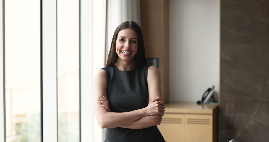 Positive Latin business woman, professional, manager, coach posing in office for professional portrait, getting happy, cheerful, laughing, crossing arms at chest, looking at camera