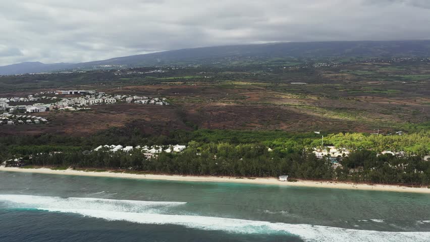 Aerial view of moody Plage des Brisants beach with waves and clouds, Saint-Gilles-Les-Bains, Reunion.