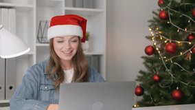 Cheerful young woman in a Santa hat is joyfully celebrating the holidays by using a laptop for a virtual gathering. The festive atmosphere includes Christmas decorations and a holiday spirit - Powered by Shutterstock - Get 15% off with code: PIKWIZARD15