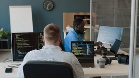 Rear view of unrecognizable Caucasian man working on cybersecurity codes in modern office, his Black colleague giving him digital tablet - Powered by Shutterstock - Get 15% off with code: PIKWIZARD15