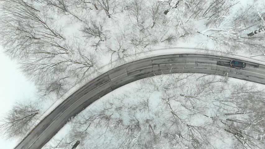 Beautiful aerial top-down view of snow covered pine forest and a road winding among trees. Rime ice and hoar frost covering trees. Scenic winter landscape near Vilnius, Lithuania.