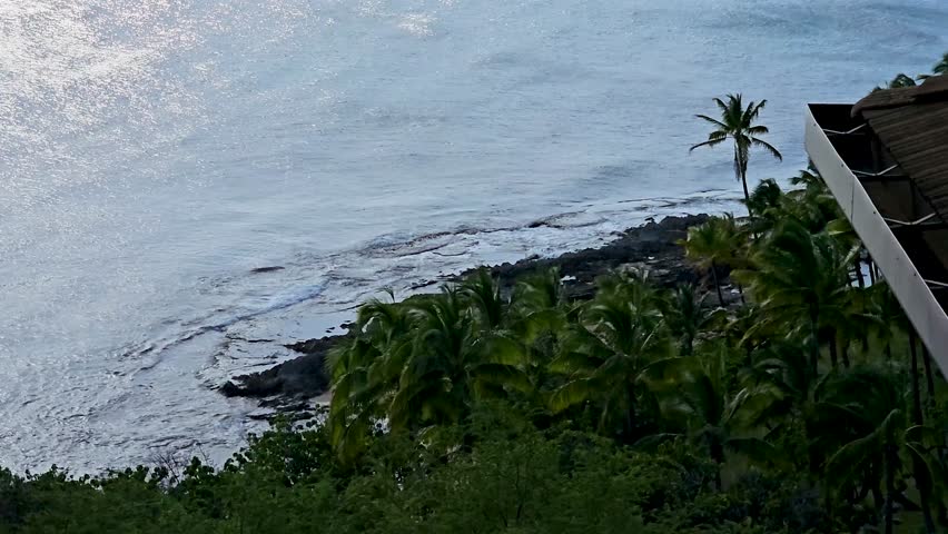 footage of the Pacific ocean at sunset with waves, lush green trees, plants and grass, blue sky and clouds on the island of Oahu at the Ko Olina Resort in Kapolei Hawaii USA