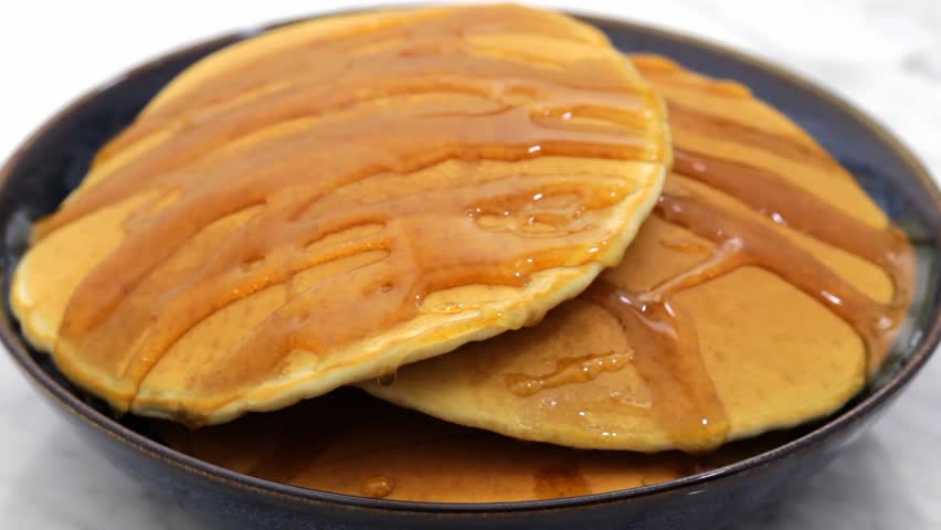 Pouring sweet delicious maple syrup on top of pancakes pile.