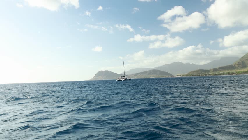 footage sailing in a boat off the coast of the island of Oahu at sunset with blue ocean water, waves, blue sky and clouds in Kapolei Hawaii USA