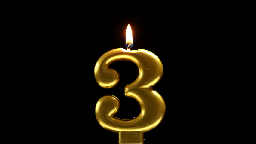 Golden number 3 birthday candle burning against a black background, creating a sleek and elegant celebration scene.