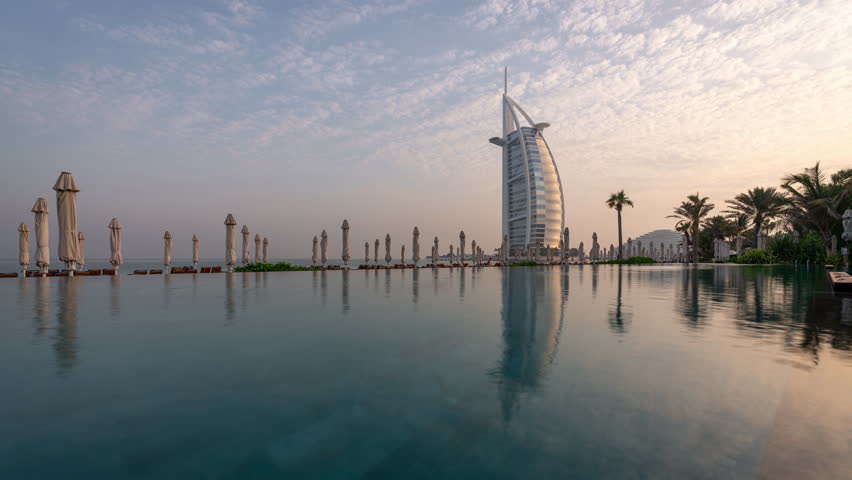 Burj Al Arab hotel in Dubai, UAE reflecting in a pool a sunny morning. Time lapse clip
