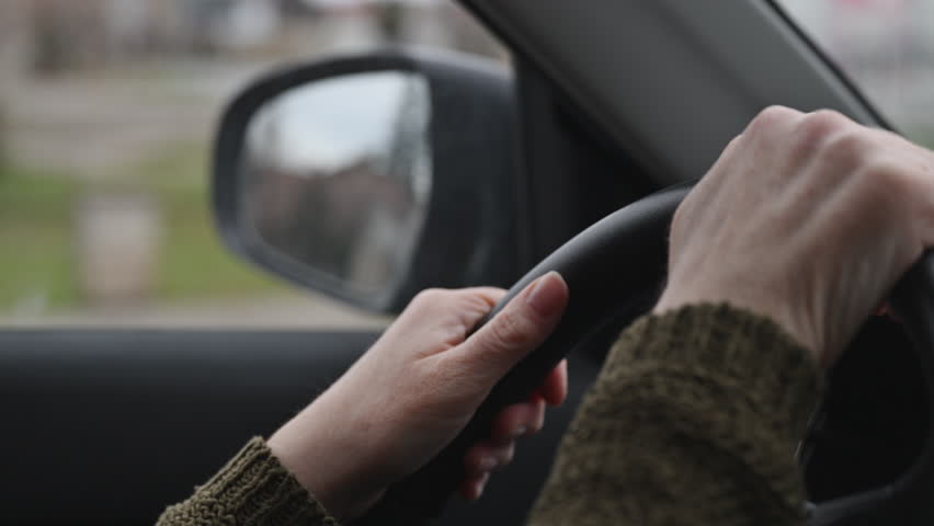Turning left on road intersection, closeup of female hands on steering wheel, selective focus