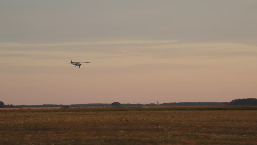 A light-engine airplane is coming in for landing and lands in a field. The action takes place against the background of a bright and large setting sun.