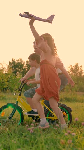 Father teaches children to ride bike in park at sunset. Daddy, kids play together outdoors. Dad teaches little boy, girl to ride children bike on road in spring. Happy family. Child cyclist smiling