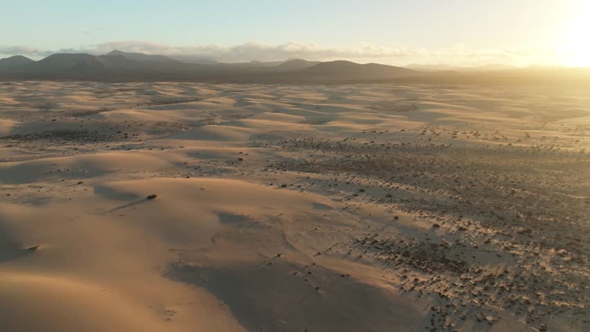 Aerial view of beautiful sand dunes under a serene sunset with mountainous terrain, Parque Natural de Corralejo, Fuerteventura, Canary Islands, Spain.
