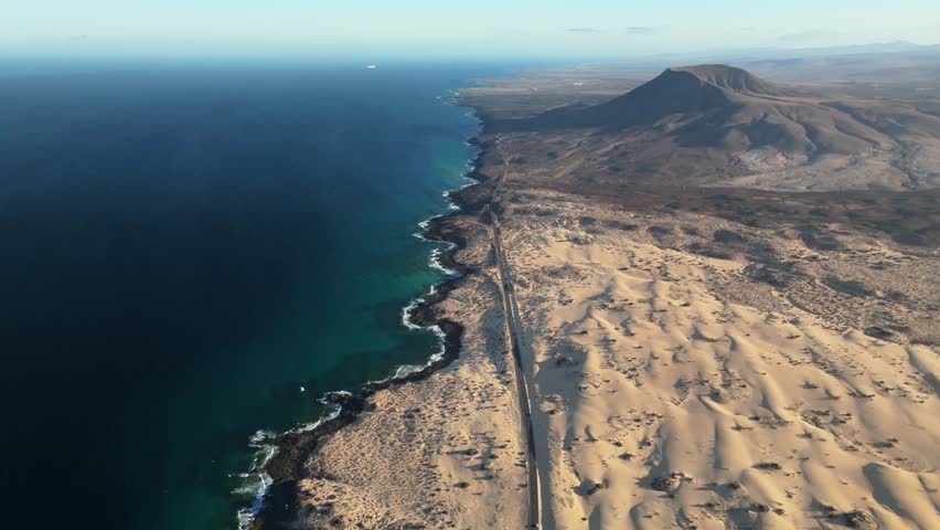 Aerial view of beautiful sand dunes and expansive coastline by the serene ocean, Parque Natural de Corralejo, Fuerteventura, Spain.