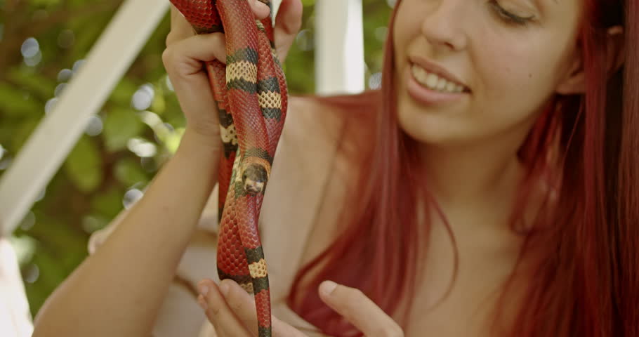 A woman with red hair holds her pet snake outdoors on a sunny day.
