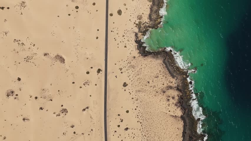 Aerial view of tranquil sandy beach and blue ocean with rocky coastline and dunes, Parque Natural de Corralejo, Fuerteventura, Spain.
