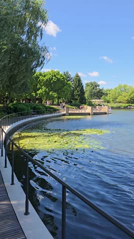 panning footage of a rippling lake with lush green trees, plants and grass, blue sky, clouds and people at Chicago Botanic Garden in Glencoe Illinois USA