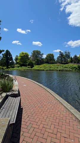 panning footage of a rippling lake with lush green trees, plants and grass, blue sky, clouds and people at Chicago Botanic Garden in Glencoe Illinois USA