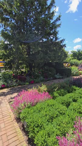panning footage of colorful flowers, lush green trees, plants and grass, people walking and a water fountain, blue sky and clouds at Chicago Botanic Garden in Glencoe Illinois USA