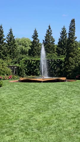 Glencoe Illinois USA 8 10 2024: panning footage of colorful flowers, lush green trees, plants and grass, people walking and a water fountain, blue sky and clouds at Chicago Botanic Garden in Glencoe I