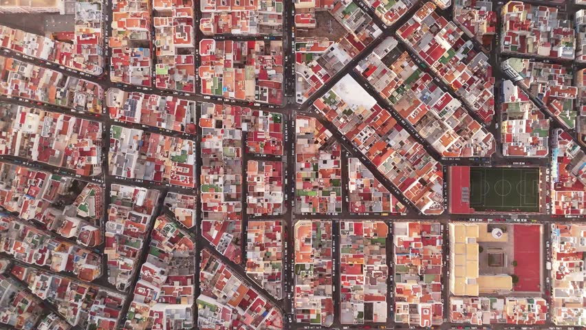 Aerial view of vibrant rooftops and a soccer field in a dense urban landscape, Las Palmas de Gran Canaria, Spain.