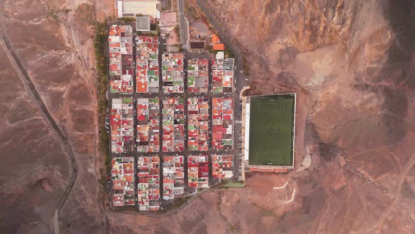 Aerial view of Las Coloradas Stadium surrounded by colorful houses in a scenic desert landscape, Las Palmas de Gran Canaria, Spain.