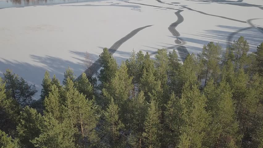 Aerial view of a frozen ice lake with beautiful patterns and serene shadows surrounded by snowy trees, Lycksele, Sweden.