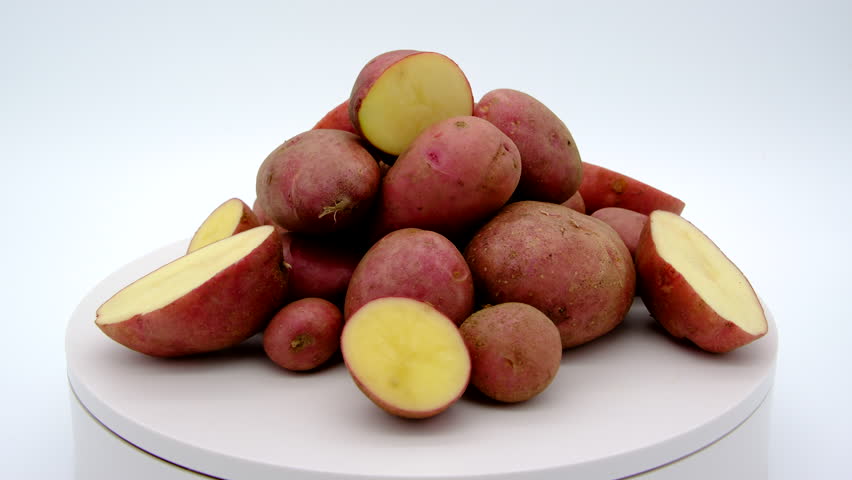 Freshly harvested from backyard organic garden pile of whole red potatoes and some sliced in half spinning or rotating on turntable against white background