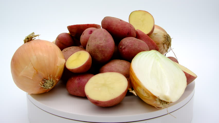 Whole and sliced in half large yellow onions and red potatoes freshly harvested from backyard garden or local farm spinning or rotating on turntable against white background