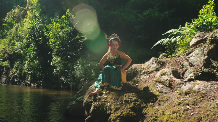A young girl in traditional attire sits by a serene riverbank surrounded by lush greenery. Sunlight filters through the trees, creating a magical atmosphere.