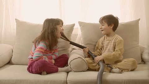 Adorable laughing kids playing at home with vacuum cleaner.