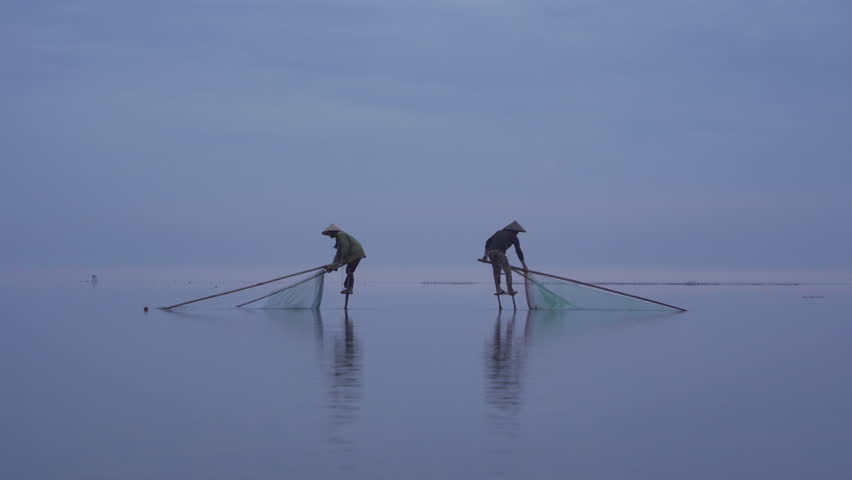 Silhouette of Vietnamese fisherman holding a net for catching freshwater fish in nature lake or river with reflection in morning time in Asia in Vietnam. People.