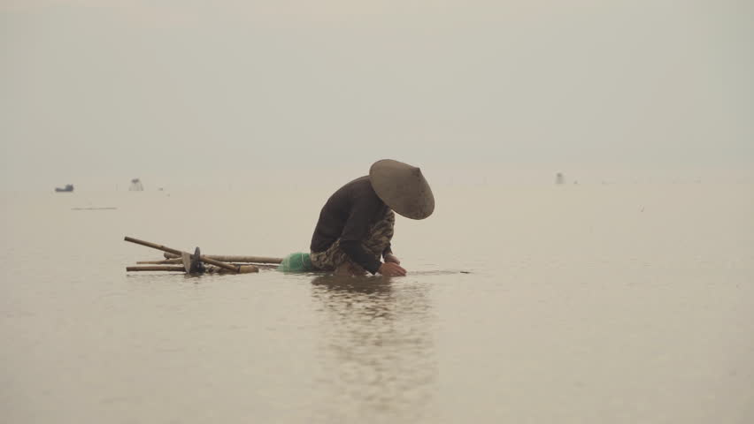 Silhouette of Vietnamese fisherman holding a net for catching freshwater fish in nature lake or river with reflection in morning time in Asia in Vietnam. People.
