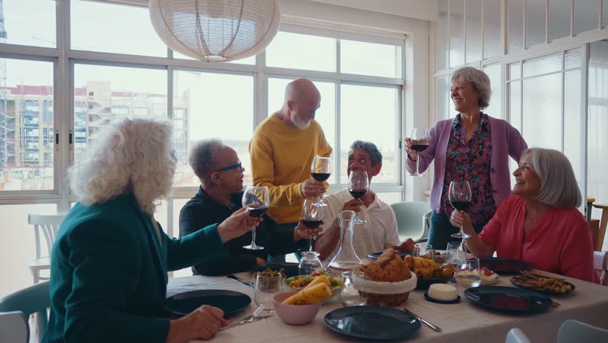 Cinematic footage of a group of seniors eating in a beautiful house apartment. Old friends reunited, having fun remembering stories and sharing good food. Concept about seniority.