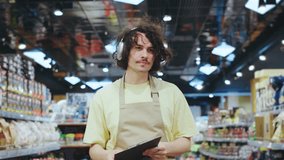 A young male employee at a grocery store is seen holding a clipboard while standing in the aisle. He is engaging with customers, checking inventory, and ensuring the store runs smoothly - Powered by Shutterstock - Get 15% off with code: PIKWIZARD15