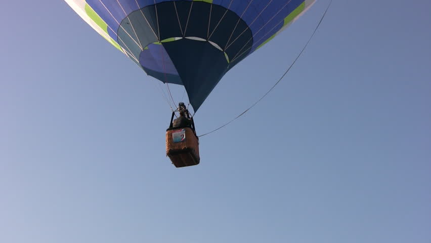 Hot air balloon blue-yellow-white color with a wicker basket soars in the