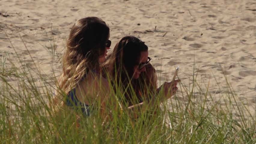 Two women are relaxing and sunbathing on the beach, lying on the warm sand. The scene captures a peaceful moment of leisure and enjoyment under the sun.